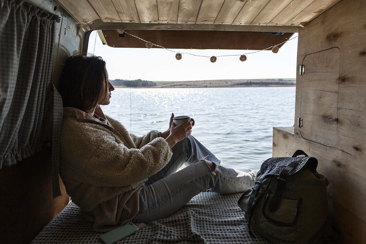 kobieta siedzi wewnątrz kampera nad wodą 