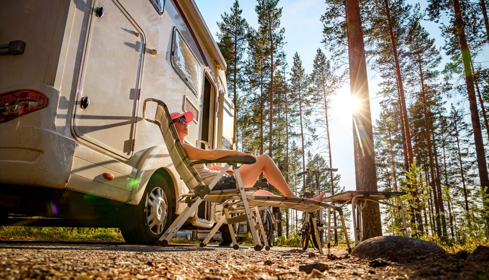 Kobieta w lesie siedzi na leżaku obok kampera