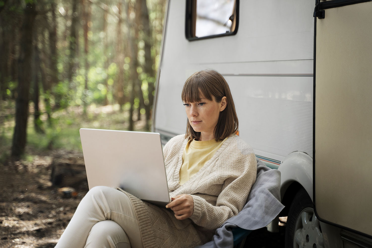 Kobieta siedzi obok kampera z laptopem na nogach